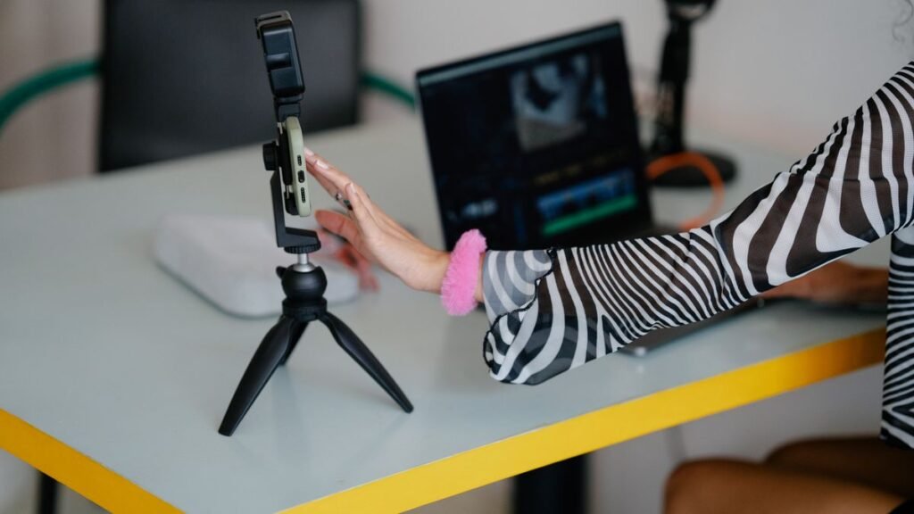 Creator setting up a smartphone on a tripod next to a laptop for editing